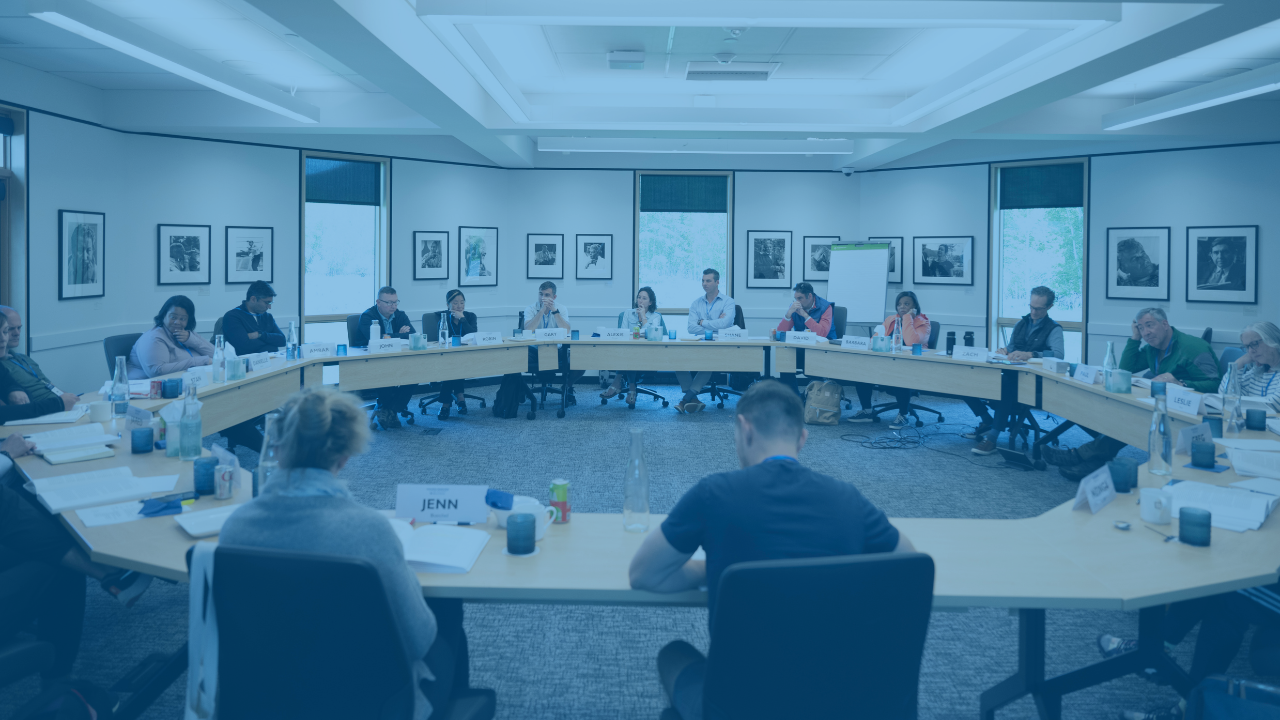 A group of seminar participants sit in a circular arrangement at a roundtable, engaged in discussion.