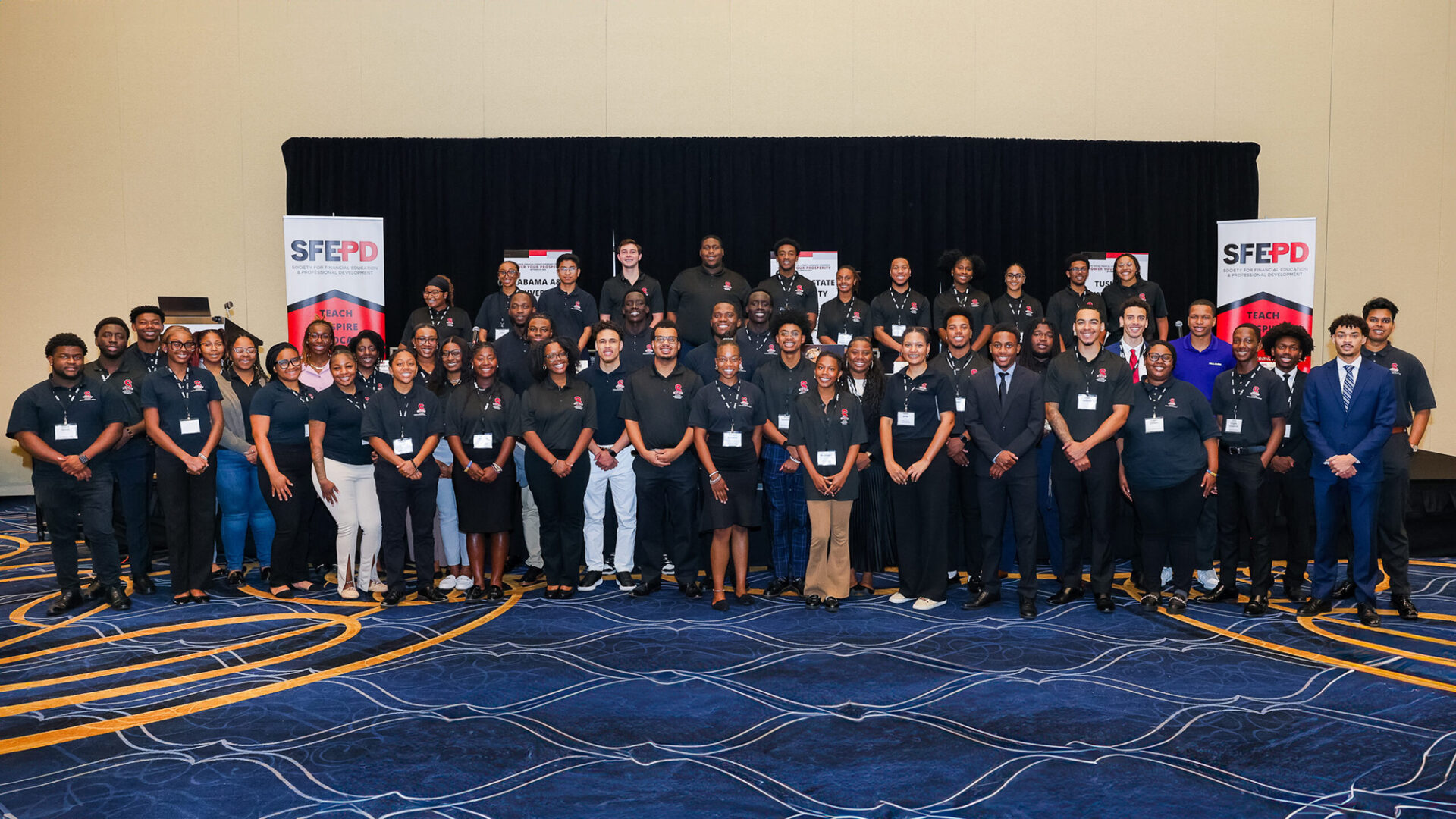 A group of over 50 students pose for a photo in front of a stage at a conference.