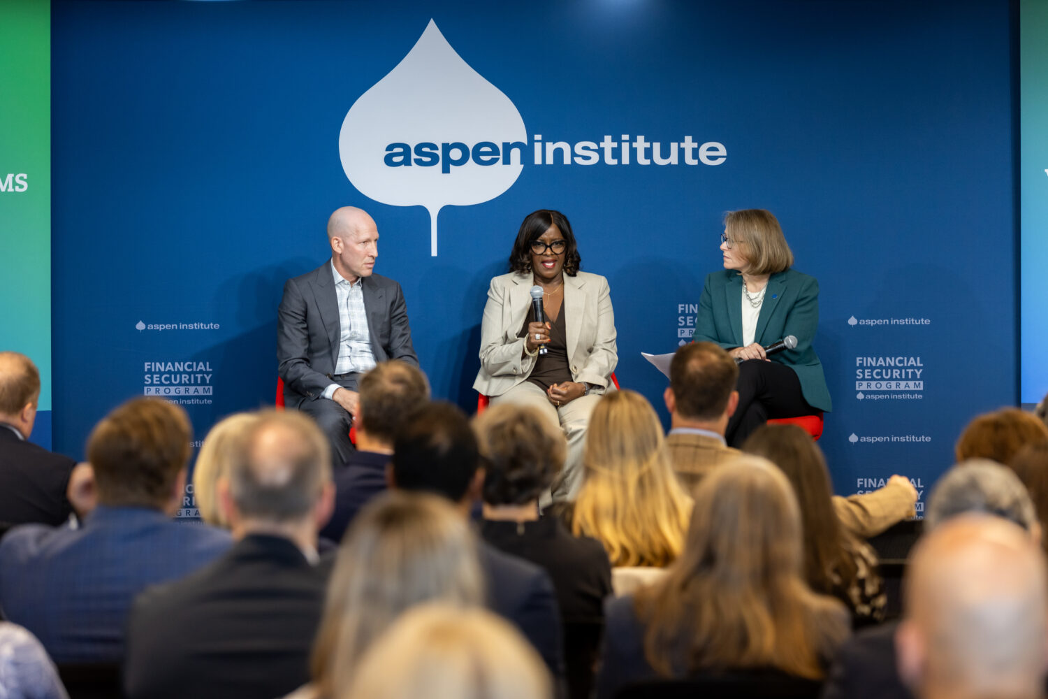 A panel speaks before a large crowd in front of an Aspen Institute Backdrop.