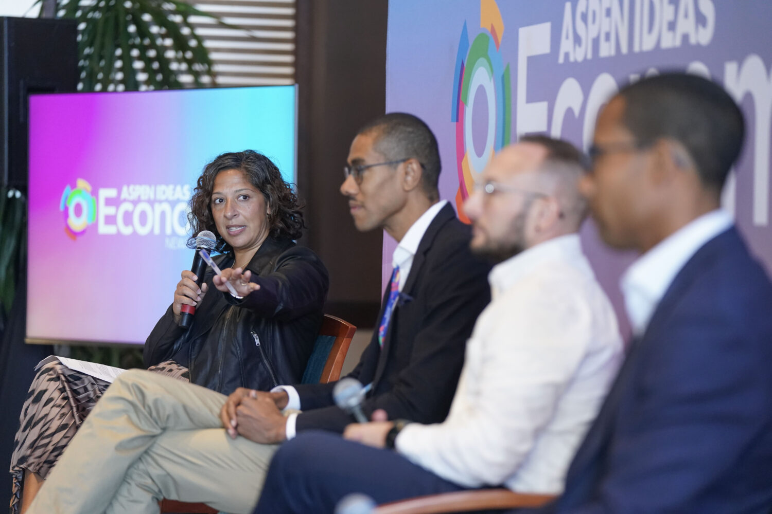 Joanna Smith-Ramani holds a microphone and facilitates a panel with three other people at Aspen Ideas: Economy