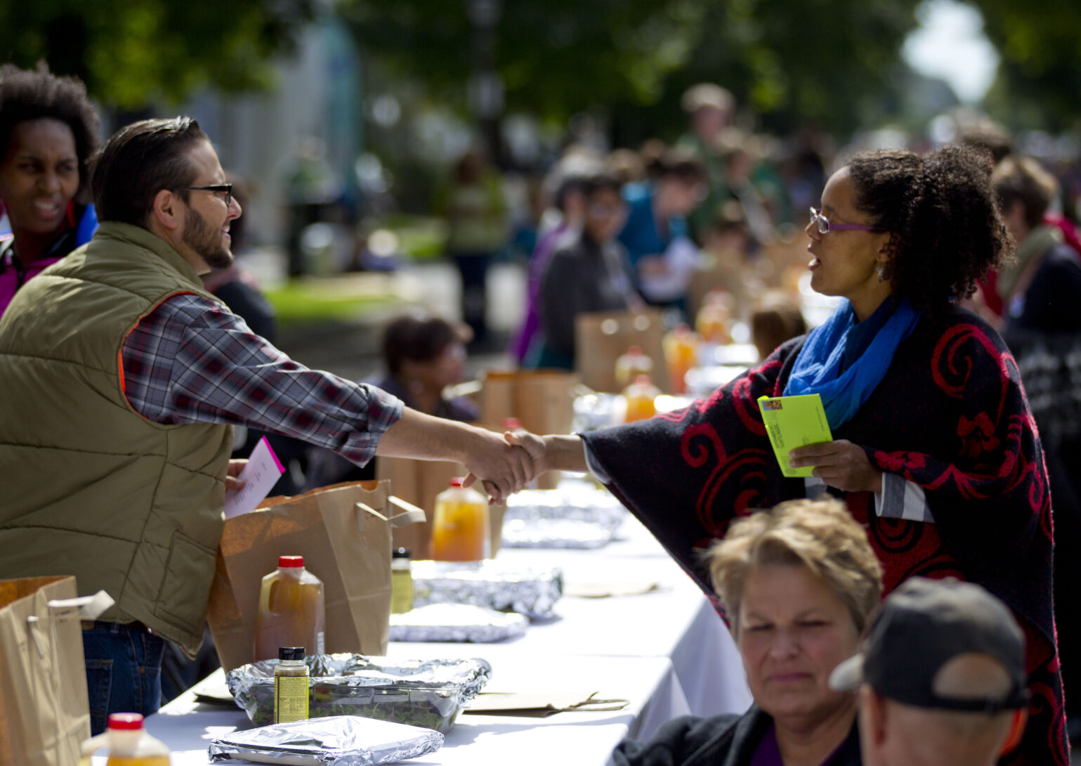 Neighbors enjoying a community meal and shaking hands. Photo credit: Andy Clayton-King